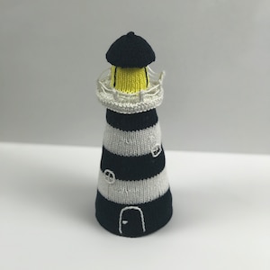 May include: A hand-knitted lighthouse toy with black and white stripes, a yellow light, and a black door.