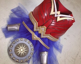 Puede incluir: Un disfraz de Wonder Woman rojo, dorado y plateado para un niño, que incluye un corpiño, un tutú, un escudo y brazaletes.