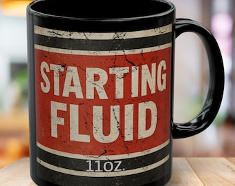 May include: Black ceramic mug with a distressed red and white label that reads "STARTING FLUID." The mug has a capacity of 11oz. and features a black handle. The design has a vintage, industrial aesthetic.