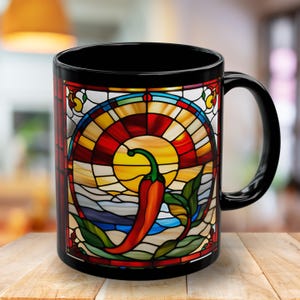 Può includere: Tazza in ceramica nera con un design a vetrata di un peperoncino rosso con foglie verdi su uno sfondo di sole giallo e rosso. La tazza ha un manico e un bordo neri e il design è incorniciato da un bordo rosso.