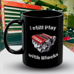 Könnte beinhalten: Schwarze Kaffeetasse mit einer weißen Grafik eines Automotors und dem Text "I still Play with Blocks".