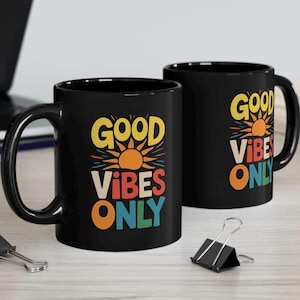 May include: Two black ceramic mugs with a white graphic design. The design features a sun with rays and the text "Good Vibes Only" in rainbow colors.