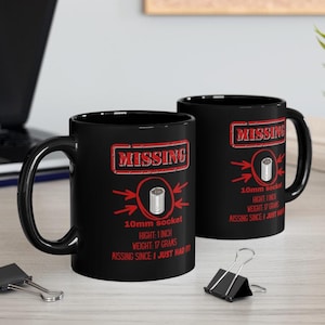 May include: Two black coffee mugs with a white design. The design says "MISSING" in red with an arrow pointing to a 10mm socket. The text below says "10mm socket, HIGHT: 1 INCH, WEIGHT: 17 GRAMS, MISSING SINCE I JUST HAD IT".