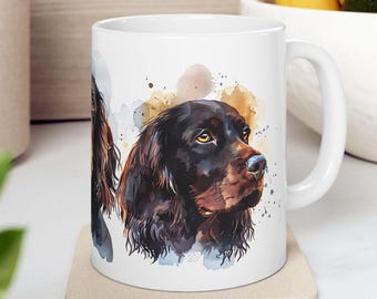 Könnte beinhalten: Weiße Keramiktasse mit einer Aquarell-Illustration eines braunen und schwarzen Gordon Setter Hundes. Der Kopf des Hundes ist zur Seite gedreht und seine Augen schauen den Betrachter an. Der Hintergrund ist hellbraun mit blauen und weißen Spritzern.
