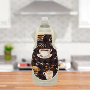 May include: A clear bottle of dish soap is adorned with a miniature apron. The apron features a brown and white coffee-themed design with the words "Java" and "Expresso" and images of coffee cups and beans. The apron has a cream-colored strap.