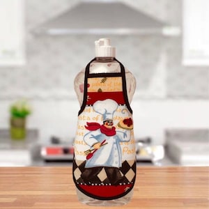 May include: A clear liquid soap dispenser adorned with a decorative apron featuring a cartoon chef. The apron has a red, white, and black color scheme with the words "Pasta of the Day". The chef holds a plate of food and a pair of utensils.