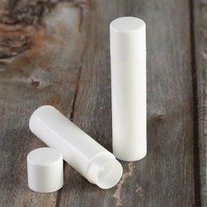 May include: Three white lip balm tubes on a wooden surface. Two tubes are closed and one tube is open, showing the inside of the tube.