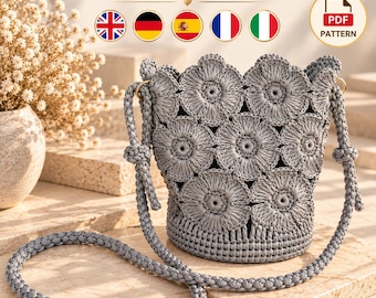Puede incluir: Un bolso tipo cubo de ganchillo gris con un patrón de motivos florales, una correa trenzada para el hombro y una base circular. El texto Floral Crochet Bag Pattern y PDF PATTERN es visible sobre el bolso, junto a cinco banderas nacionales.