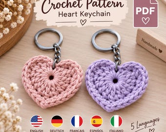 Puede incluir: Un patrón de ganchillo en PDF digital para un llavero de corazón. La imagen muestra dos corazones de ganchillo, uno rosa claro y otro morado claro, cada uno unido a una anilla de metal oscuro. El texto dice: Crochet Pattern Heart Keychain.