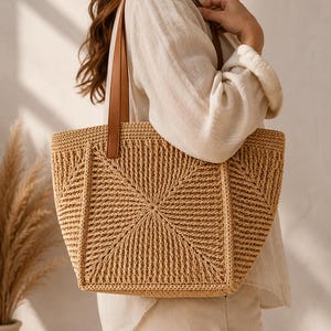 Könnte beinhalten: Beige gewebte Tragetasche mit geometrischem Muster und braunen Ledergriffen. Die Tasche wird von einer Person getragen, die ein weißes Hemd trägt. Das Design der Tasche ist strukturiert und die Farbe ist natürlich.