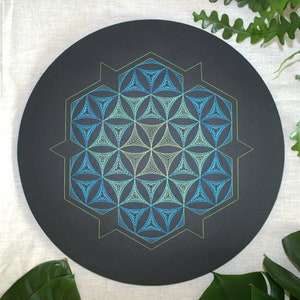 Könnte beinhalten: Ein schwarzer runder Teller mit einem geometrischen Muster in Grün und Blau. Das Muster ist ein Lebensblume-Muster.