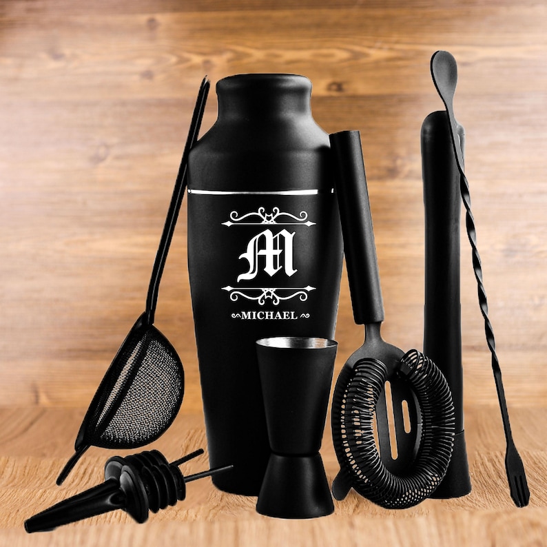 May include: A black cocktail shaker set with a personalized design. The set includes a shaker, strainer, jigger, muddler, bar spoon, and pour spouts. The shaker is engraved with the letter "M" and the name "MICHAEL".