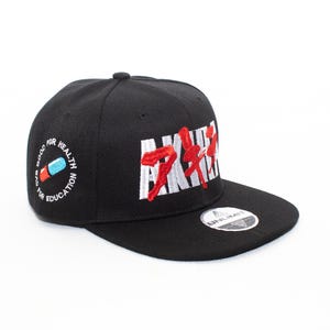 Può includere: Cappellino da baseball nero con la scritta "XXX" ricamata in bianco e rosso. Il cappellino ha una visiera piatta e una piccola toppa con la scritta "UNLIMIT". Il lato del cappellino riporta la scritta "GOOD FOR HEALTH EDUCATION" con un'immagine di pillola.