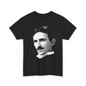 Puede incluir: Camiseta negra con un retrato en blanco y negro de Nikola Tesla. La imagen muestra a Tesla con bigote y cabello oscuros. La camiseta es de cuello redondo.
