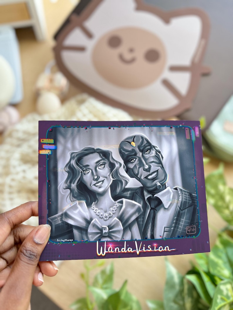 May include: A square print featuring a grayscale illustration of two characters from WandaVision. The woman wears a dress and necklace, and the man is in a suit. The print has a purple border and the words "WandaVision" are written in gold.