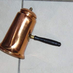 May include: A copper coffee pot with a black wooden handle. The pot has a shiny, polished finish.