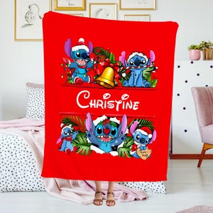 May include: A red Christmas blanket featuring Stitch from Lilo & Stitch. The blanket has multiple images of Stitch wearing a Santa hat and holding Christmas decorations. The name "Christine" is written in white script.