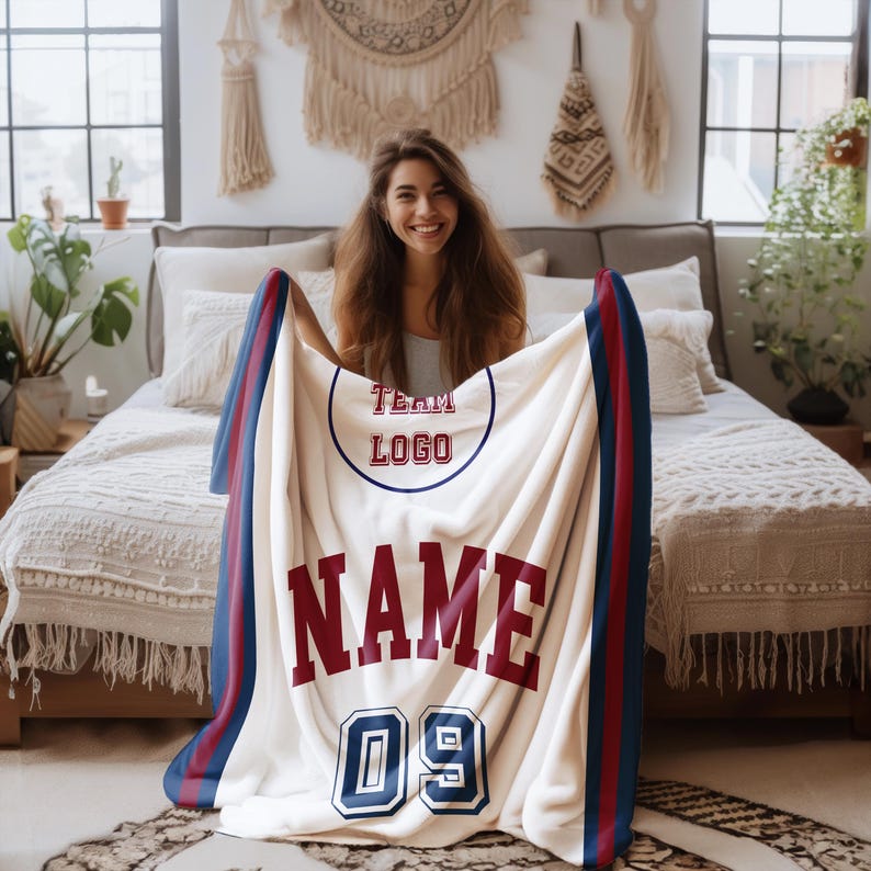 Peut inclure: Une couverture en polaire blanche avec un design de maillot rouge et bleu. La couverture pr&eacute;sente un logo d'&eacute;quipe, le mot "NAME" et le num&eacute;ro "09".