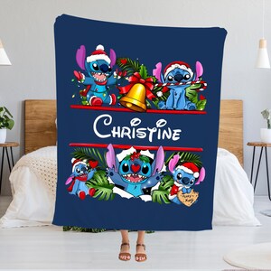 May include: A navy blue blanket featuring the character Stitch in a Christmas theme. The blanket has the name "Christine" in white script. Stitch is depicted wearing a Santa hat and surrounded by festive decorations.