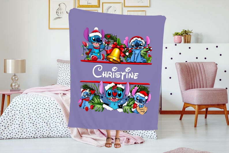 May include: A lilac blanket with Stitch characters wearing Santa hats and festive decorations. The blanket has the name "Christine" in white script. The design includes a gold bell and festive greenery, ideal for Christmas.