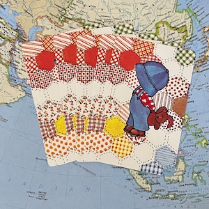 Puede incluir: Tarjeta de felicitación vintage con un diseño de patchwork, que presenta a un niño con overoles y un perro. La tarjeta tiene un patrón hexagonal con acentos rojos, blancos y amarillos. El fondo es un mapa.