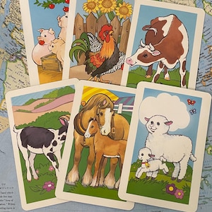 May include: A collection of vintage farm animal flashcards. Each card features a colorful illustration of a different farm animal, including pigs, a rooster, a cow, a goat, horses, and sheep. The cards are set against a light blue background.