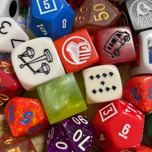 May include: A collection of polyhedral dice in various colors, including red, blue, white, and purple. The dice feature different numbers and symbols, suitable for tabletop gaming. Some dice have gold or white numbering.