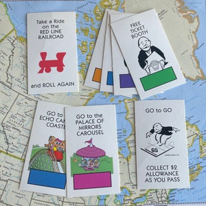 May include: A collection of Monopoly game cards featuring various locations and instructions. The cards have colorful illustrations and text, including "Free Ticket Booth" and "Go to Go". The cards are arranged on a map.