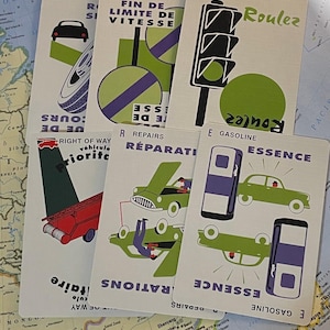 May include: A collection of vintage-style cards with automotive-themed illustrations and text. The cards feature images of a car, tire, traffic light, and gas pump, with text in English and French. The cards are arranged on a map.