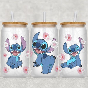 May include: Three stainless steel tumblers with a white background and a blue Stitch character from the Disney movie Lilo & Stitch. The tumblers have a bamboo lid and a straw. The Stitch character is surrounded by pink and white flowers.