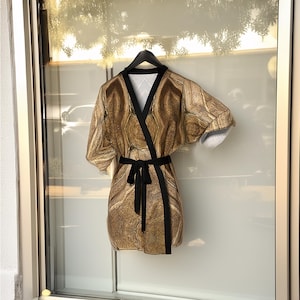 May include: A short-sleeved, gold and brown patterned robe with a black sash. The robe has a wrap-around style and a V-neck.