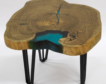 May include: A wooden coffee table with a live edge top and a turquoise blue epoxy resin inlay. The table has black metal hairpin legs.