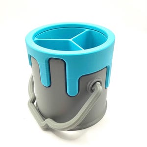 May include: A grey paint can shaped desk organiser with a blue lid and three compartments. The lid has a dripping paint effect.