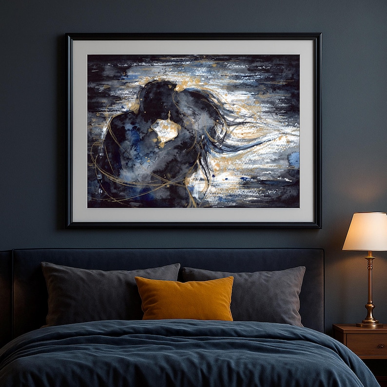 Op de afbeelding: Een ingelijste kunstdruk met een abstract aquarel van twee omhelzende silhouetten. Het kunstwerk gebruikt diep marineblauwe, zwarte en witte tinten met metallic gouden accenten die in een vloeiende beweging rond de figuren wervelen.