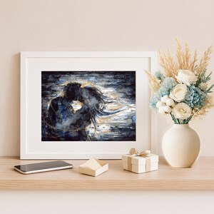 Op de afbeelding: Een ingelijste horizontale kunstdruk met een donkerblauw en zwart abstract silhouet van twee omhelzende figuren, geaccentueerd met gouden verfstreken. De print staat naast een witte vaas gevuld met witte, blauwe en gedroogde beige bloemen.