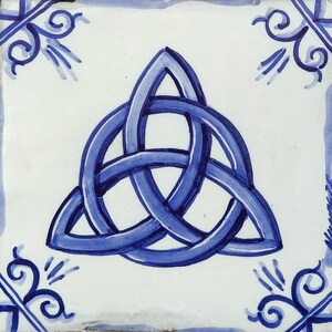 May include: Square ceramic tile featuring a hand-painted blue Celtic knot design. The knot is central on a white background, with blue decorative corner accents. The tile has a rustic, handcrafted appearance.