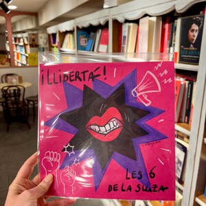 Może przedstawiać: Różowy plakat z czarną gwiazdą i czerwonymi ustami z zębami. Plakat głosi "¡LLIBERTÀ!" i "LES 6 DE LA SUIZA".