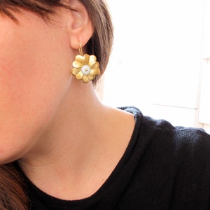 May include: Gold flower-shaped earrings with a white pearl center.