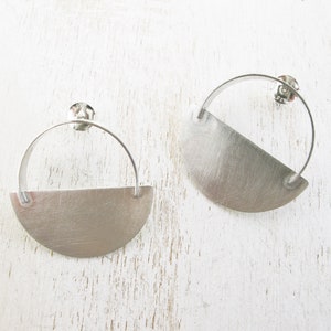 May include: A pair of silver earrings with a half-circle design. The earrings are made of a brushed metal and have a simple, modern style.