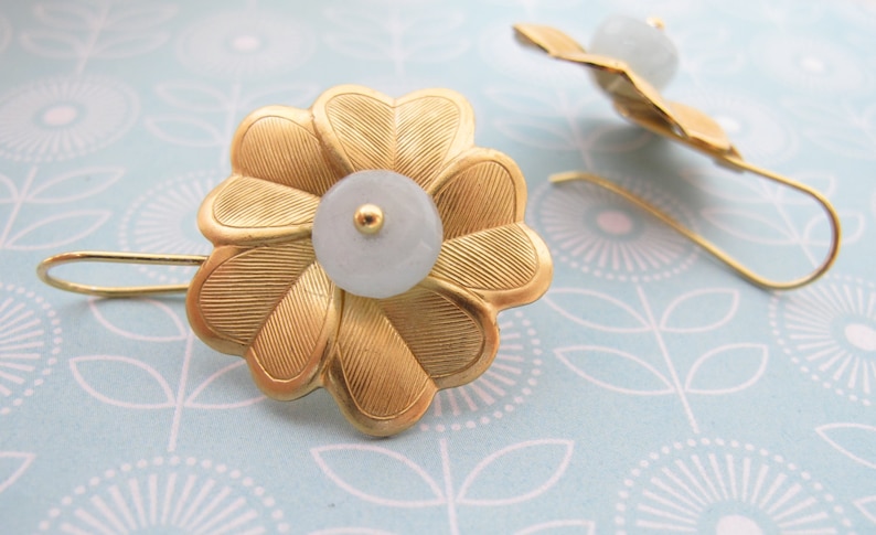May include: A pair of gold flower-shaped earrings with a light blue stone in the center of each flower.
