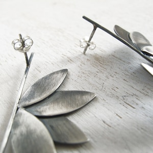 May include: A pair of silver earrings with a geometric design. The earrings are made of multiple overlapping pieces of metal that form a flower shape.