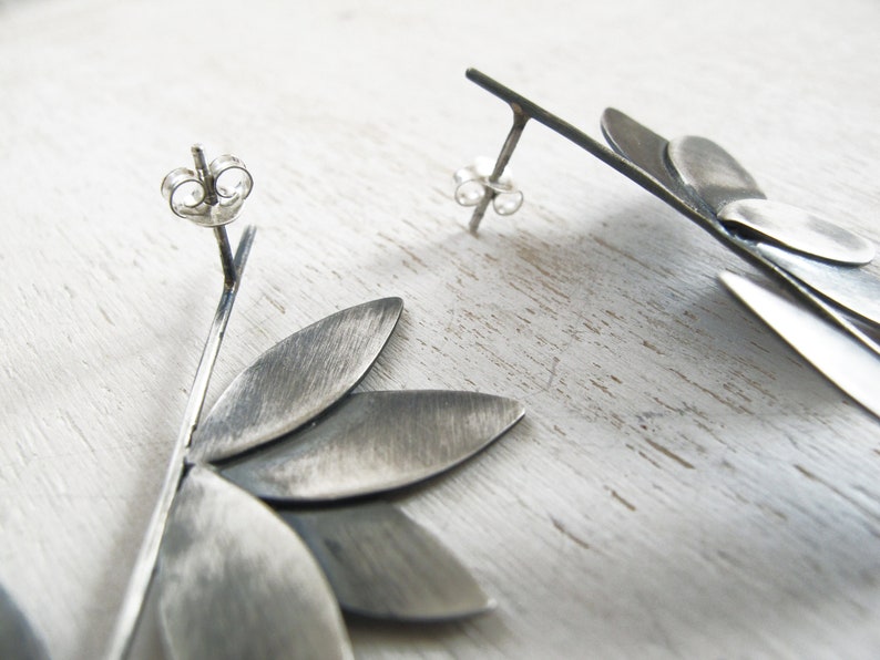 May include: A pair of silver earrings with a geometric design. The earrings are made of multiple overlapping pieces of metal that form a flower shape.