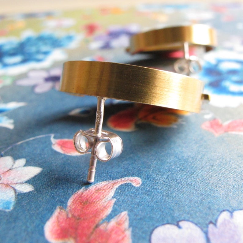 May include: A pair of gold hoop earrings with a brushed finish. The earrings have a silver post and butterfly back.