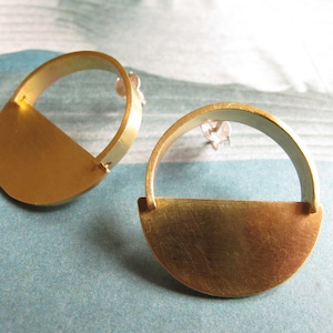 May include: A pair of gold earrings with a half-circle design. The earrings are made of brass and have a simple, modern style.