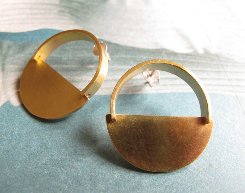 May include: A pair of gold earrings with a half-circle design. The earrings are made of brass and have a simple, modern style.