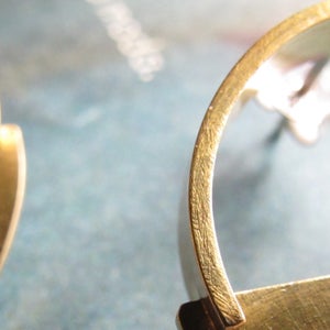 May include: A pair of gold-toned earrings with a simple, modern design. Each earring features a curved, open hoop with a flat, rectangular bar attached to the bottom.