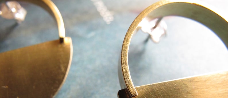 May include: A pair of gold-toned earrings with a simple, modern design. Each earring features a curved, open hoop with a flat, rectangular bar attached to the bottom.