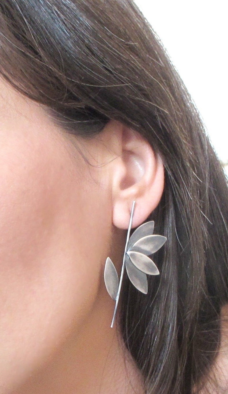 May include: Silver earrings with a leaf design. The earrings are long and dangle from the earlobe. The leaves are made of metal and have a textured surface.