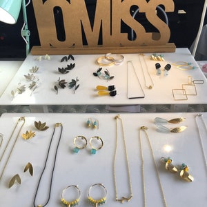 May include: A display of gold and silver jewelry, including earrings, necklaces, and bracelets. The jewelry is arranged on a white surface with a wooden sign that reads "LOMISS".