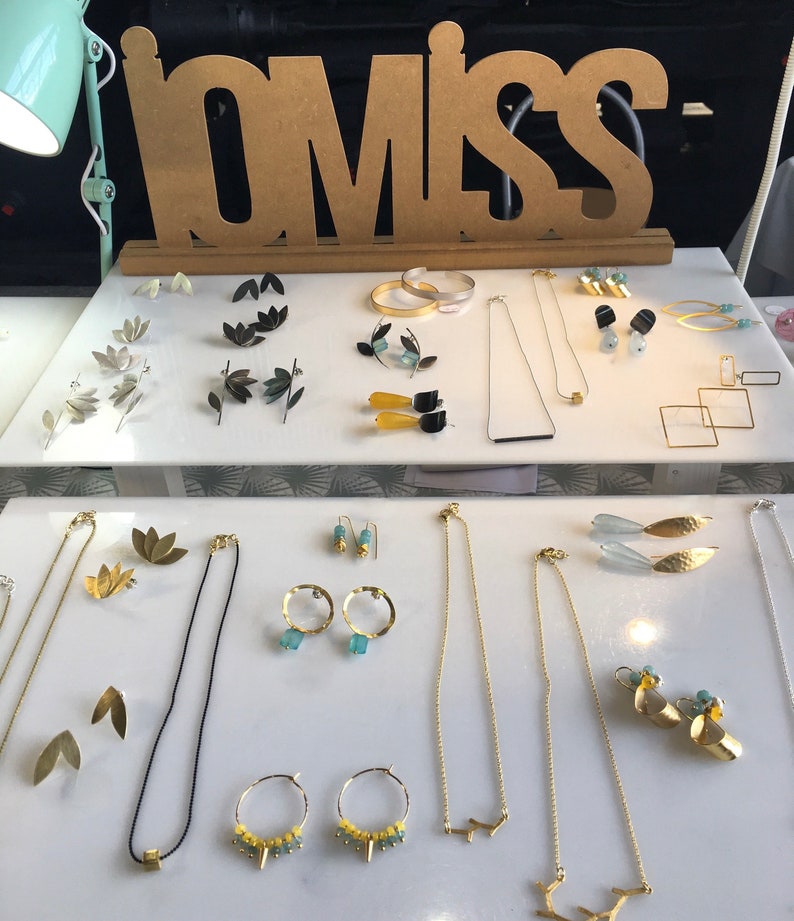 May include: A display of gold and silver jewelry, including earrings, necklaces, and bracelets. The jewelry is arranged on a white surface with a wooden sign that reads "LOMISS".